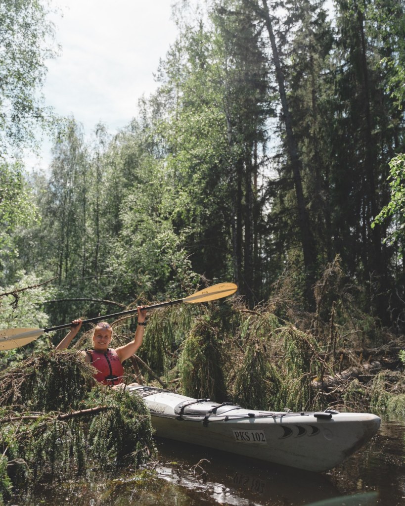 Meri yksikkökajakilla ylittämässä joen yli kaatunutta puunrunkoa